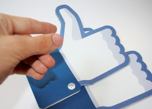 A hand picking up real life mock-ups of the Facebook Like button