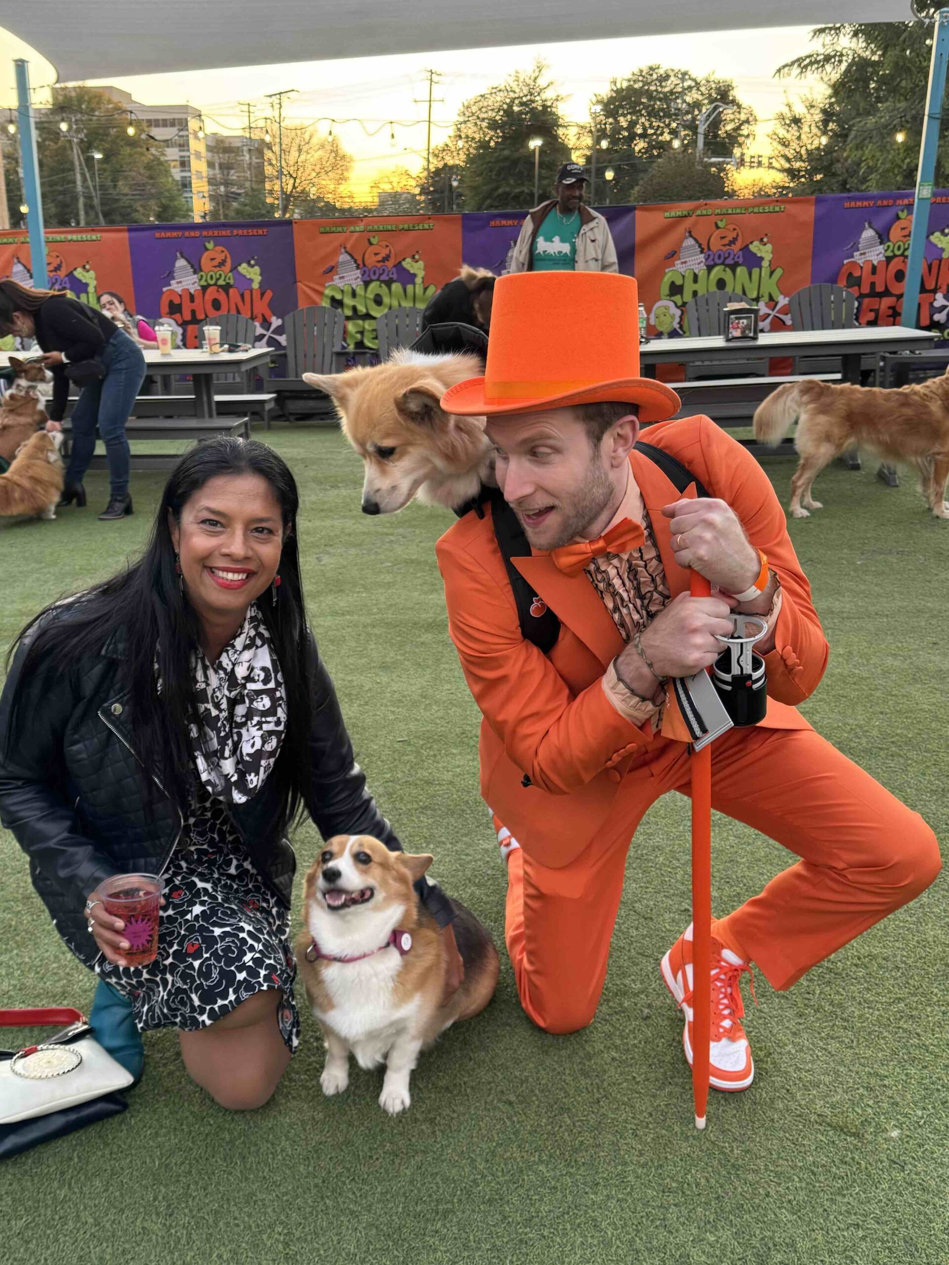 Shonali Burke kneeling, Pickles the corgi, and Maxine the fluffy corgi in a backpack on her dad's back at Bark Social, a dog park in Bethesda, Md.